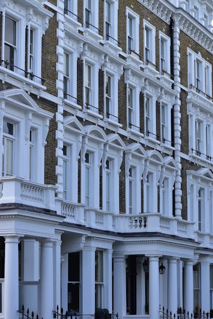 Exterior view of a historic multi-storey building with ornate white architectural details including decorative window frames, cornices, and balconies, set against a clear sky. The building features large, evenly spaced windows with black iron railings and a columned entrance. The façade is predominantly made of brick with white accents, and the lighting highlights the cleanliness and well-maintained condition of the surface materials. This image emphasizes the exterior architecture typical of Pimlico SW1 flats, illustrating the importance of exterior surface cleaning and maintenance, as offered by Westminster Carpet Cleaning for deep cleaning and sanitisation of residential façades. Visible elements include the intricate decorative moldings and the well-preserved, polished surfaces, contributing to the building’s elegant appearance.